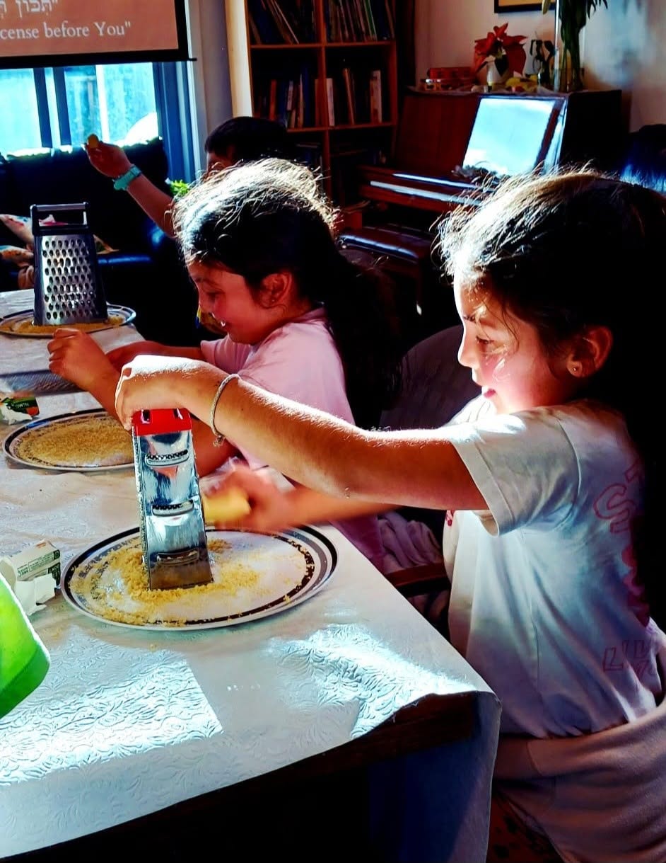 Two girls grating food onto plates at a covered table