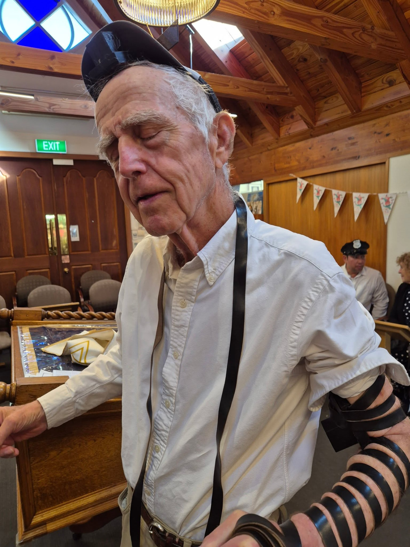 An older man wearing tefillin standing at the bimah with his eyes closed