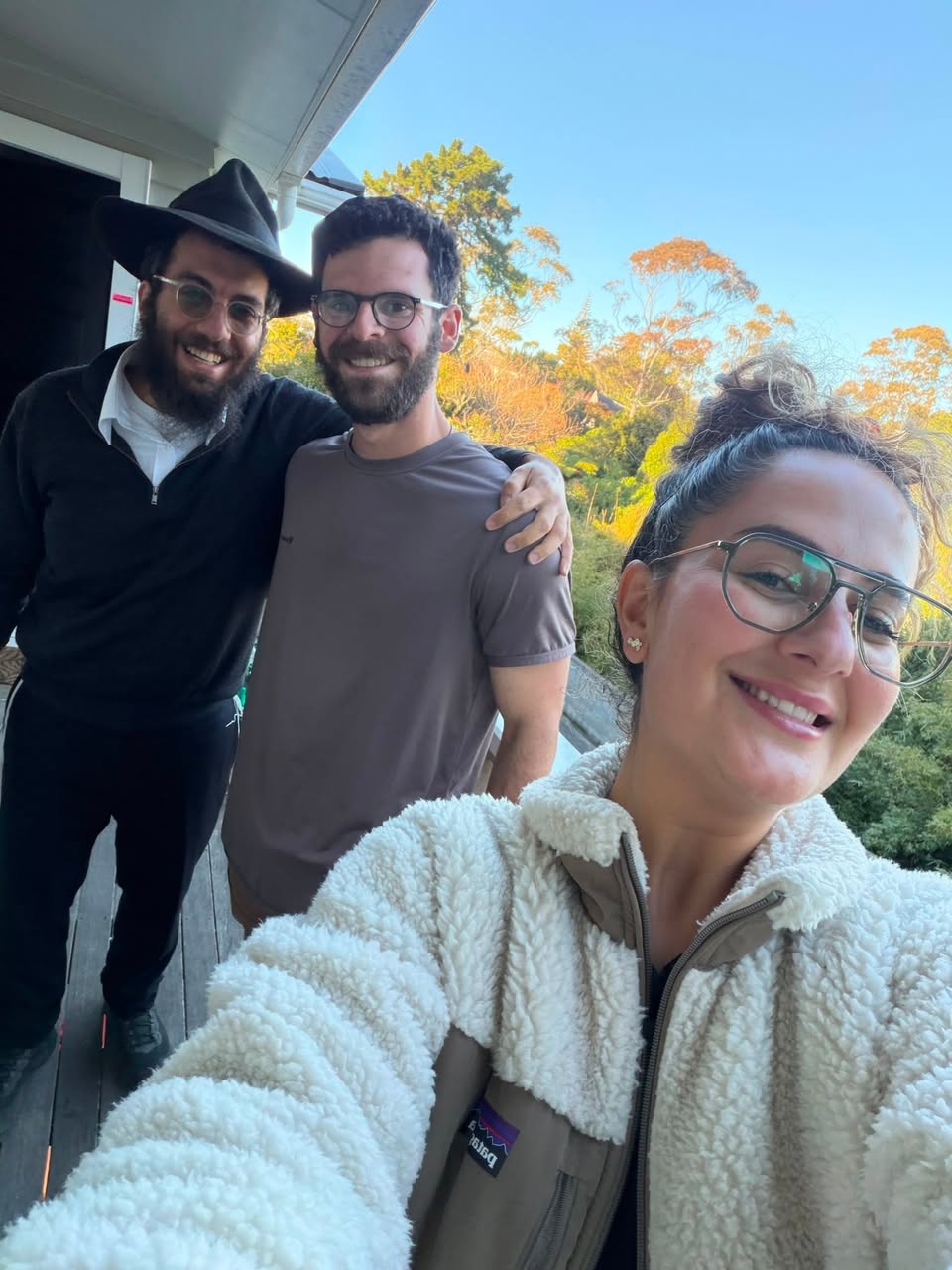 Three people smiling together on a sunlit veranda after a service