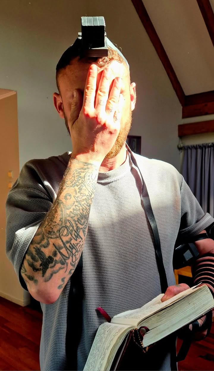 A man covering his eyes in prayer while holding an open prayer book