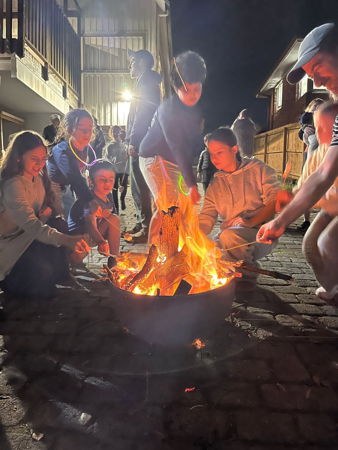 Children and adults gathered around a fire pit at night toasting marshmallows