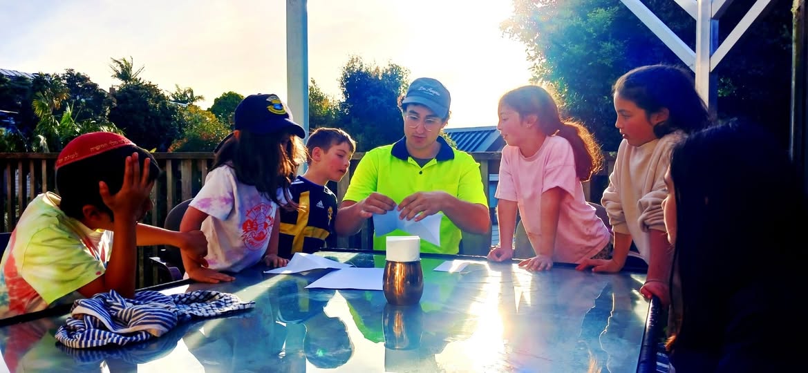 Children gathered around an outdoor table with a teacher at sunset