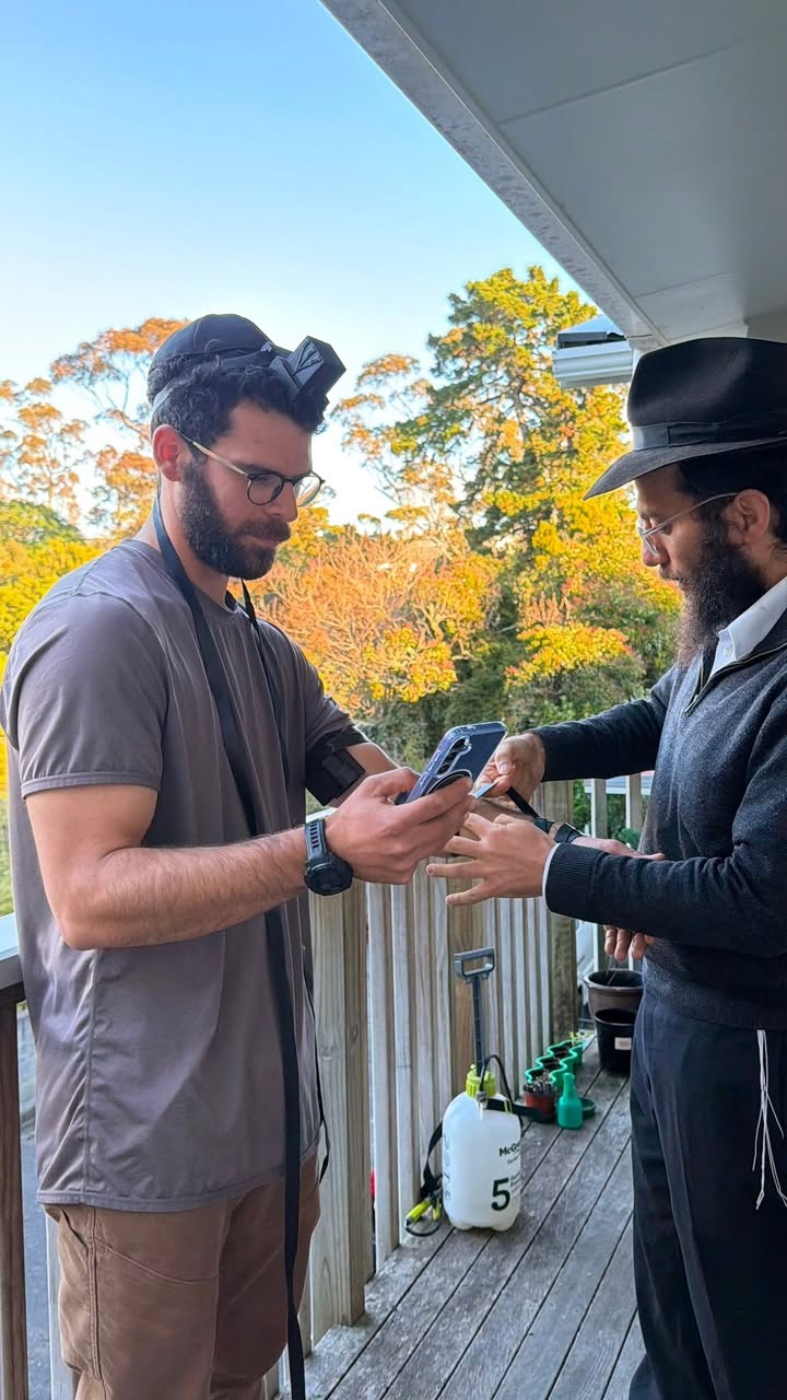 A rabbi helping a man put on tefillin on a wooden veranda