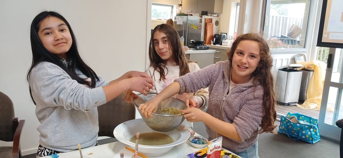 Three girls cooking together at a kitchen bench